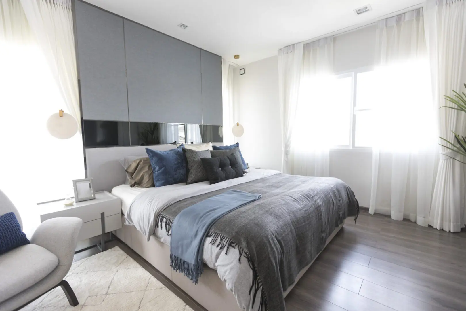 Modern white and blue bedroom with armchair by the window.