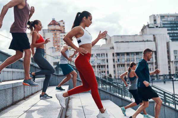 Group of young people in sports clothing jogging while exercising on the stairs outdoors